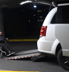 Wheelchair user Kelly Mack being helped into a wheelchair accessible Uber via a back door ramp